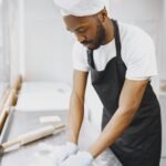 A focused baker kneading dough on a floured surface in a modern kitchen setting.